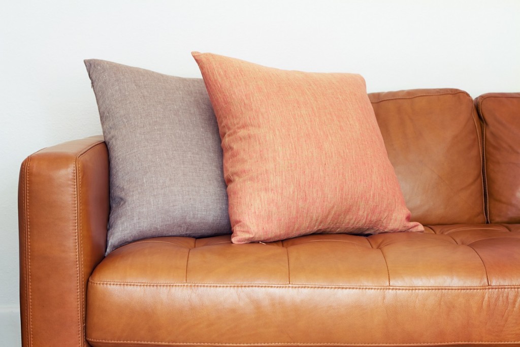 Close up of tan leather sofa with two linen cushions